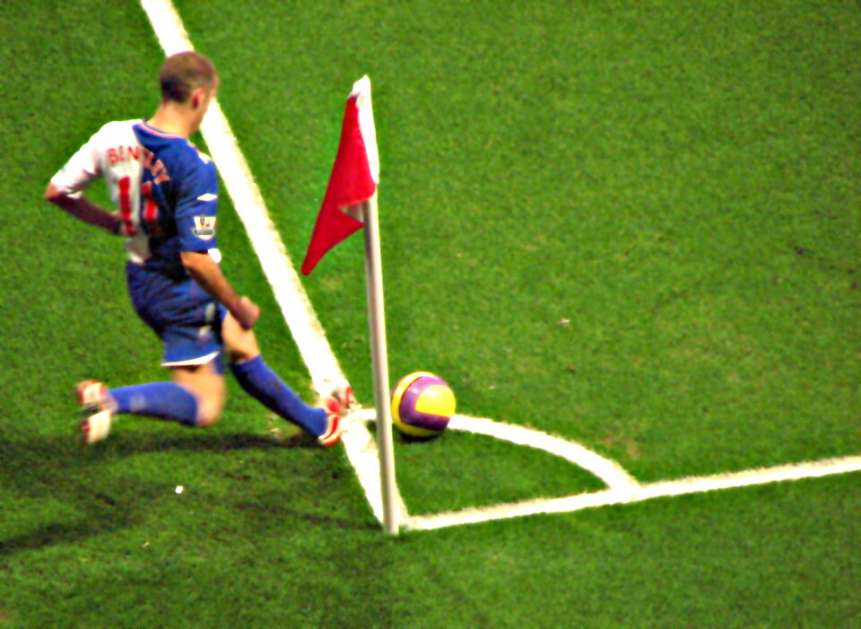 Jugador ejecutando un tiro de esquina en un partido nocturno